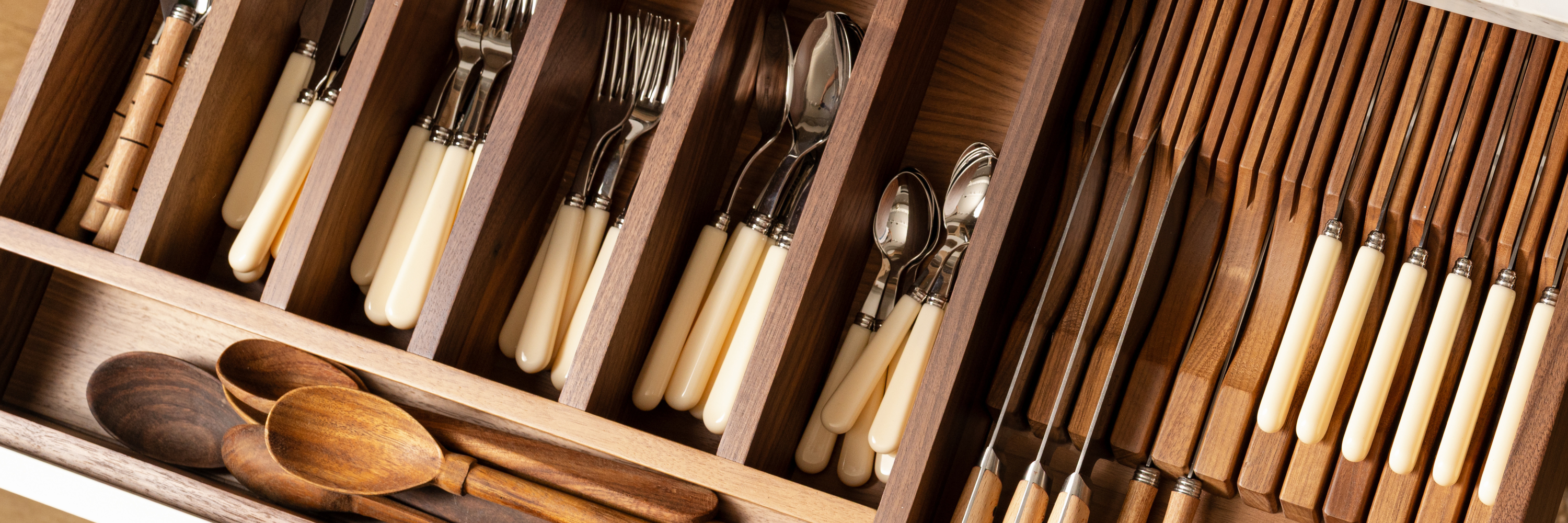 Round wooden dining table set with neutral dinnerware, linen napkins, and wildflowers in a glass pitcher. Soft light filters through linen curtains behind a cushioned bench at Calimia Home Shop.