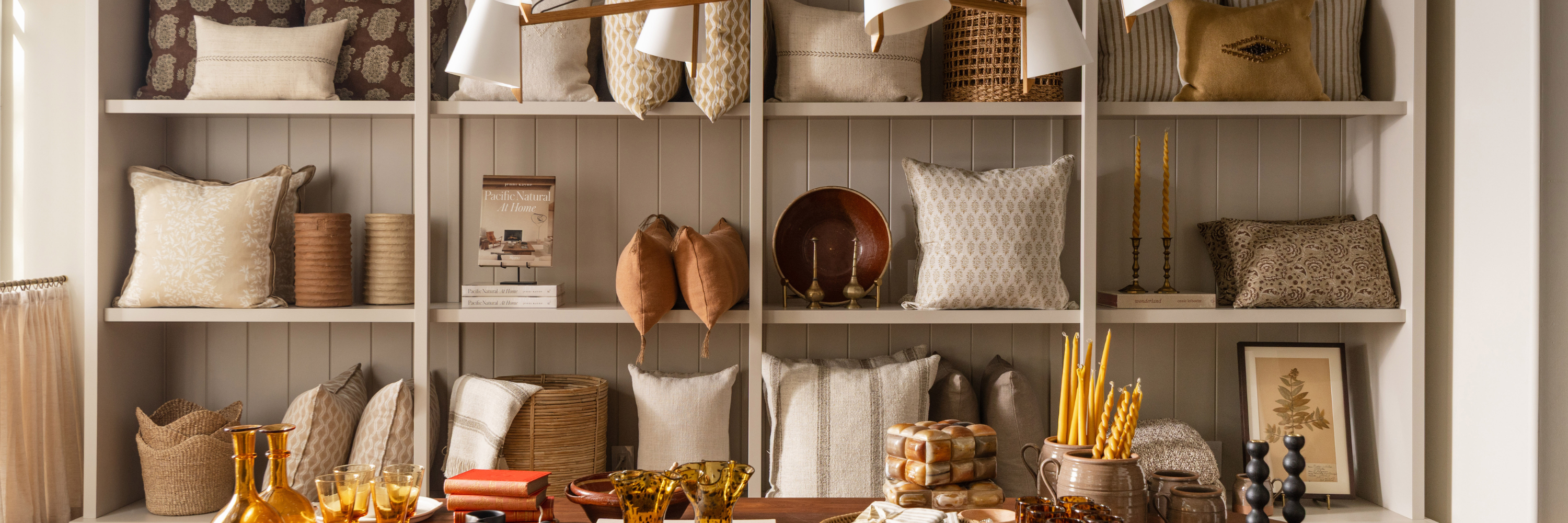 Neutral hand-embroidered and patterned pillows styled with woven baskets and decorative accents on built-in shelves at Calimia Home