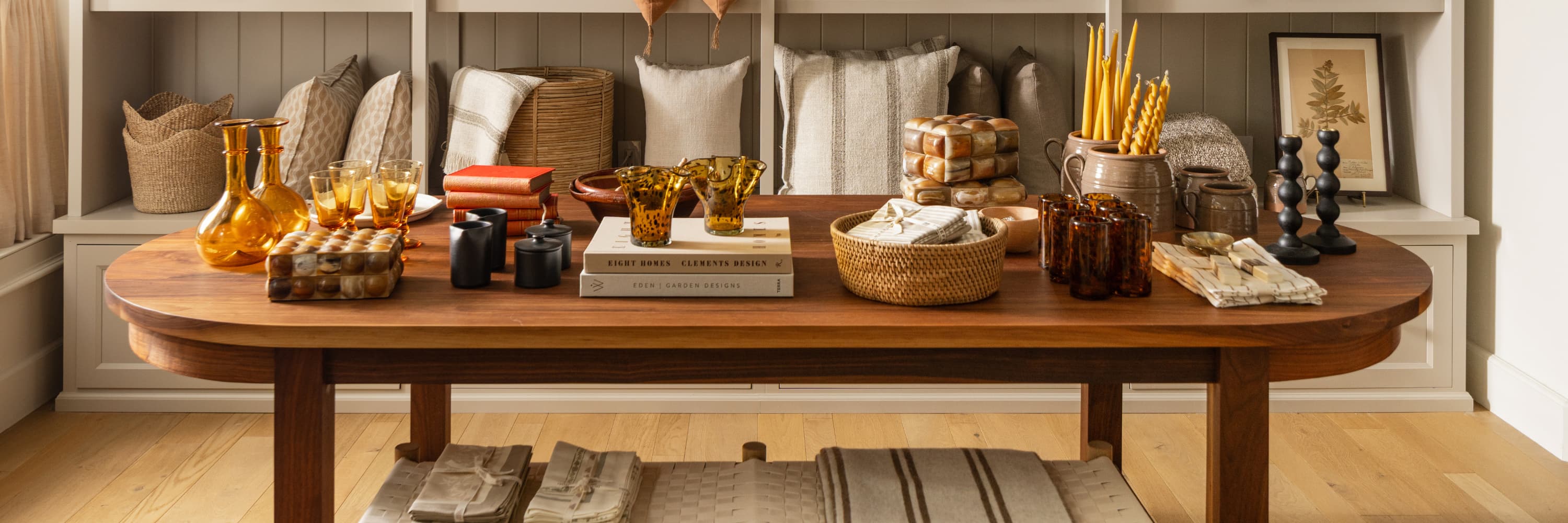 Solid oak dining table styled with amber glassware, woven baskets, linen textiles, and handcrafted decor objects at Calimia Home