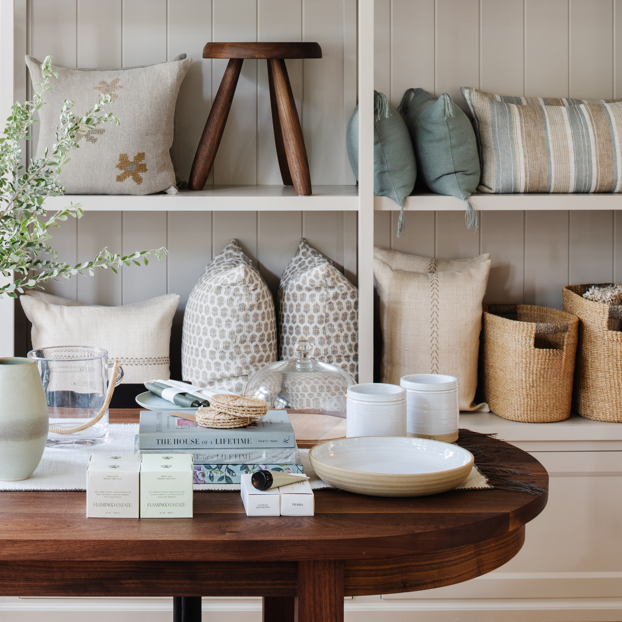 Decorative setting with pillows, books, and a wooden table against a neutral wall.