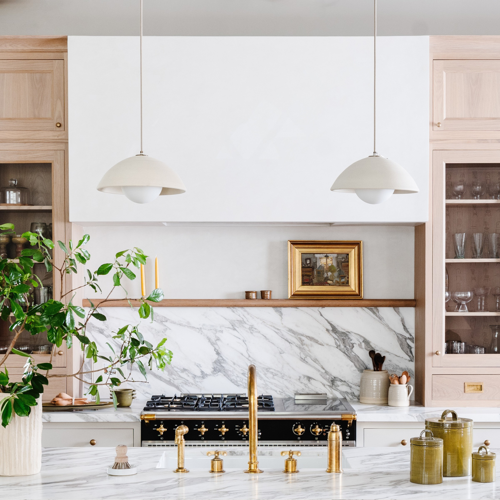 Modern kitchen with marble backsplash, brass fixtures, and 2 hanging ceramic pendants.
