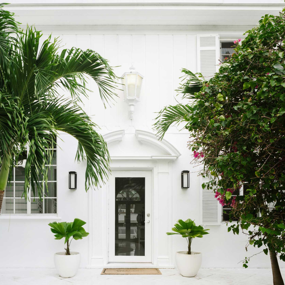 White Art Deco beach home entrance framed by palms, featured in MyDomaine