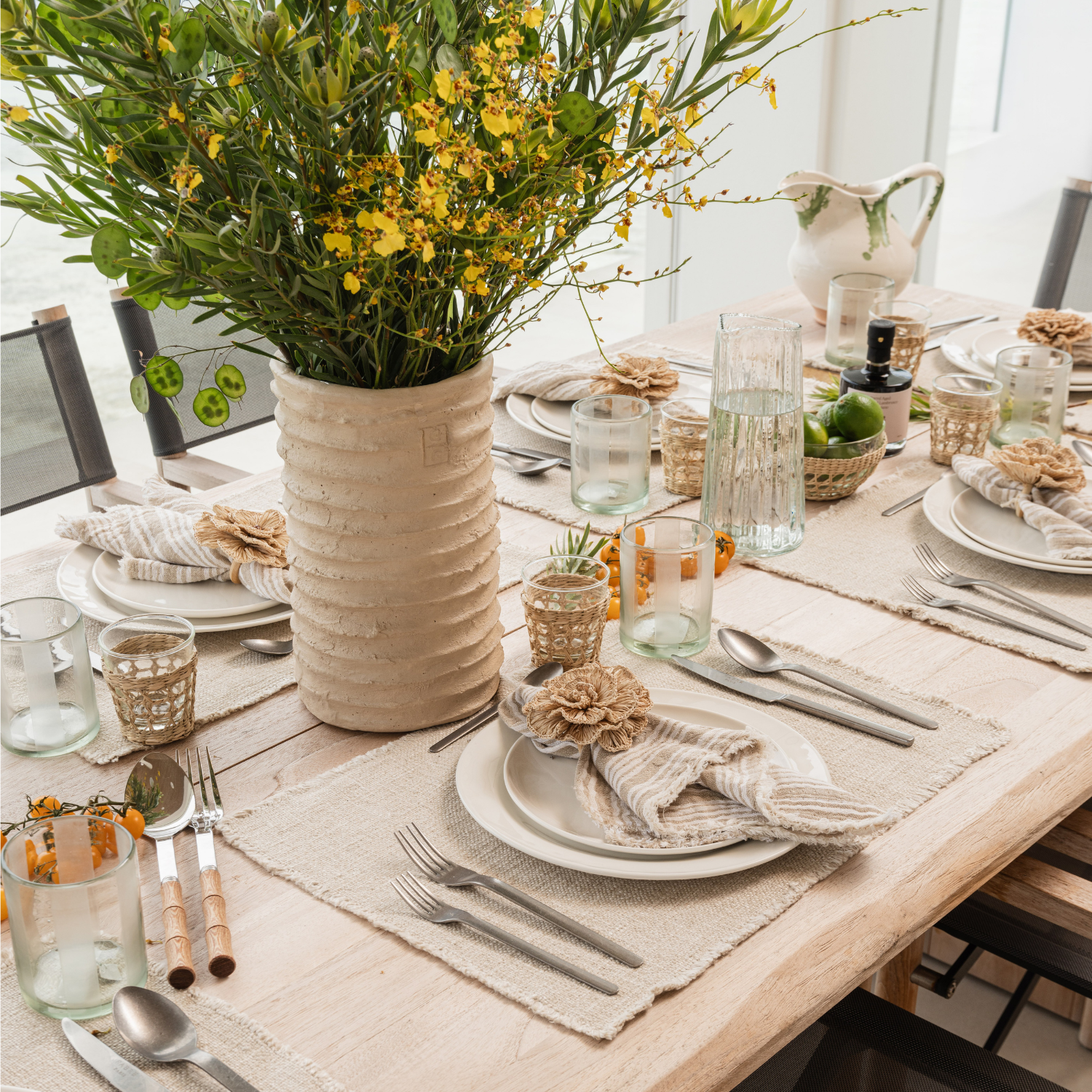 Elegant table setting with a vase of flowers, plates, and cutlery on a wooden table.