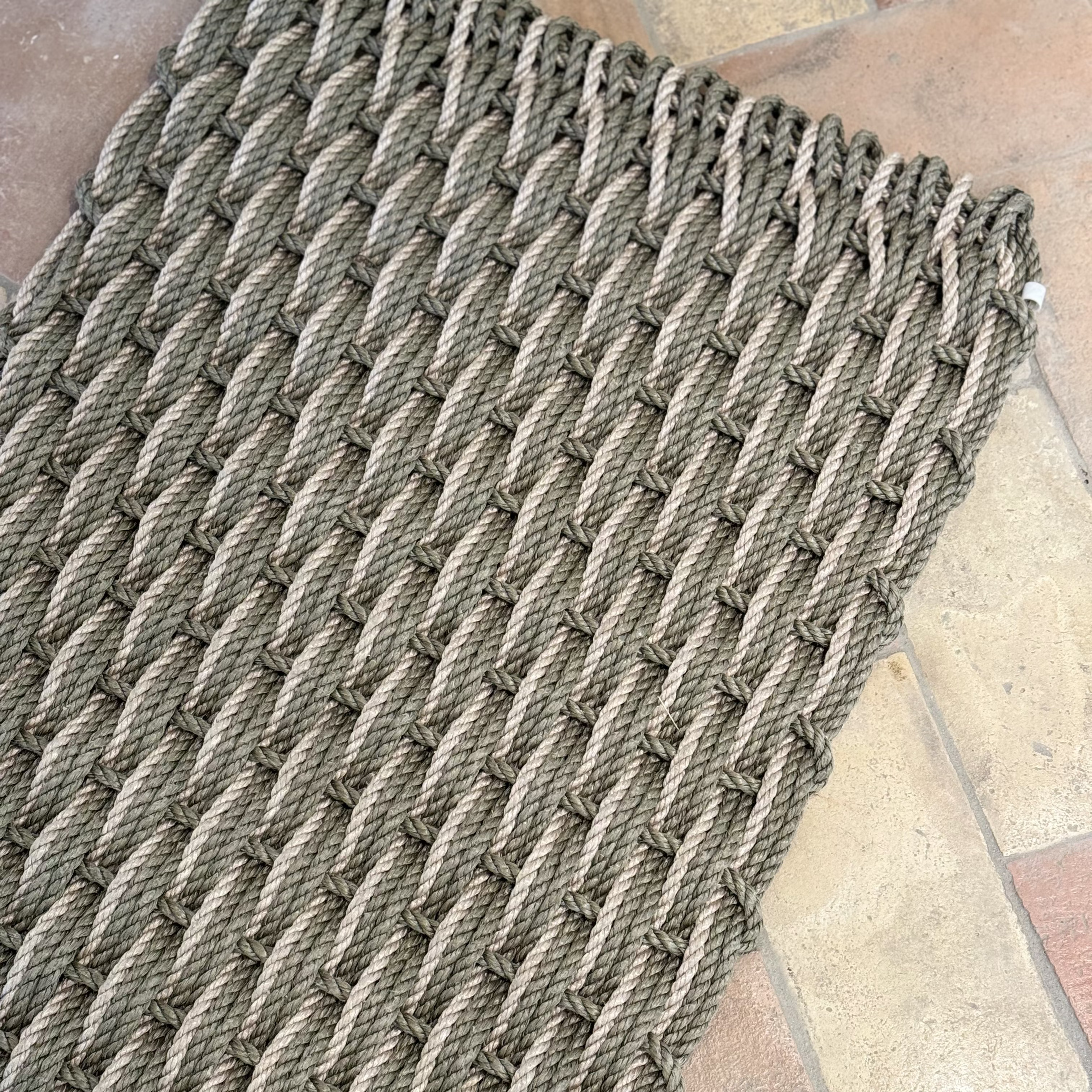 A close-up of a beige and sage green handwoven rope doormat with a textured pattern.