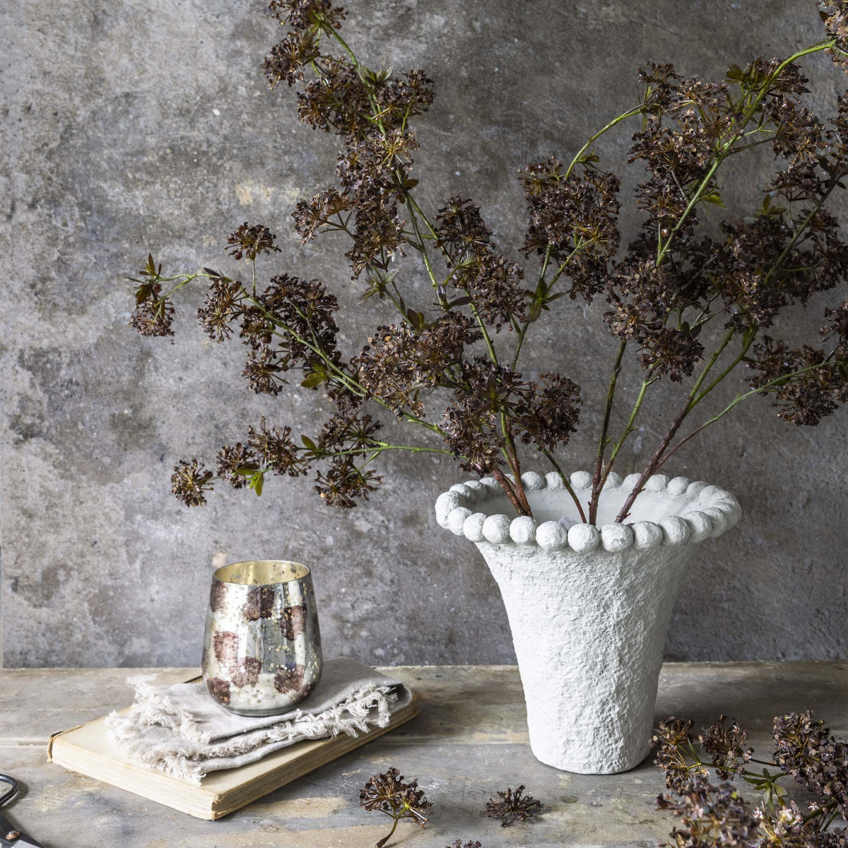 Artificial Hogweed stems by Abigail Ahern arranged in a white beaded vase on a rustic table