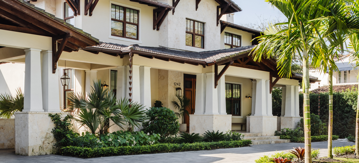 Front exterior of the Coral Way Craftsman home with tapered columns, dark trim, and tropical landscaping