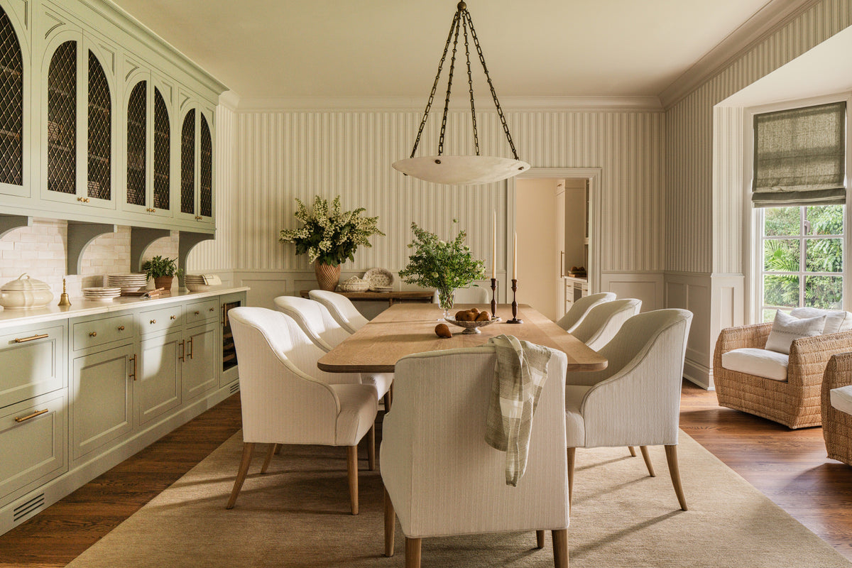 Dining room with sage green built-in cabinets, arched glass fronts, and an oak table beneath an alabaster pendant
