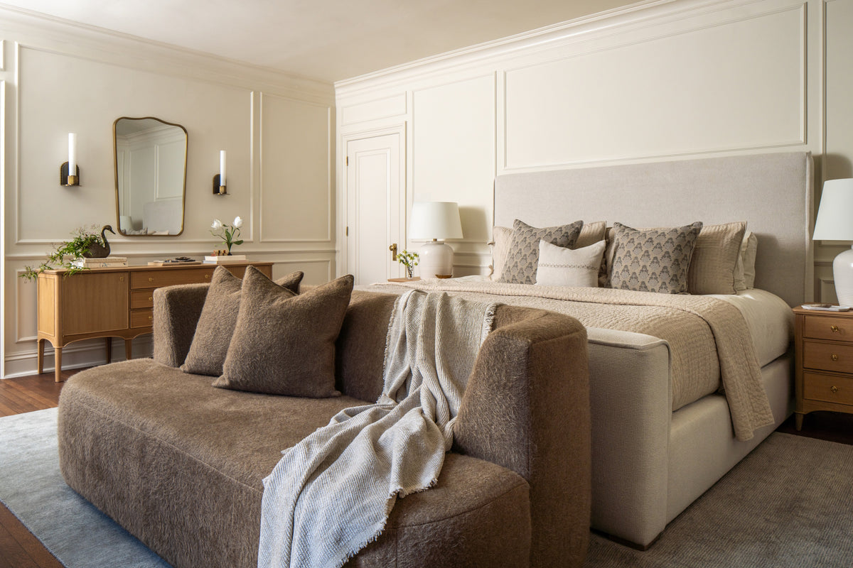 Primary bedroom with an upholstered bed, mohair settee, and wall molding in soft neutrals