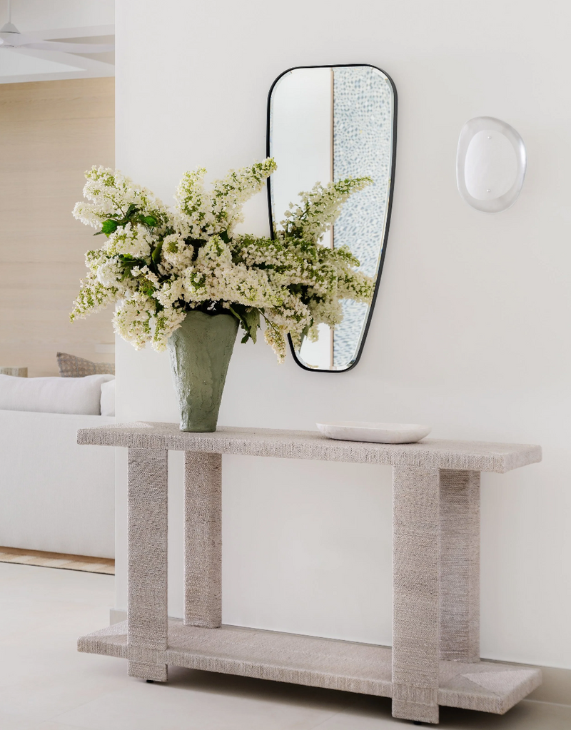 Textured limestone console styled with an organic-form mirror and white flowering branches