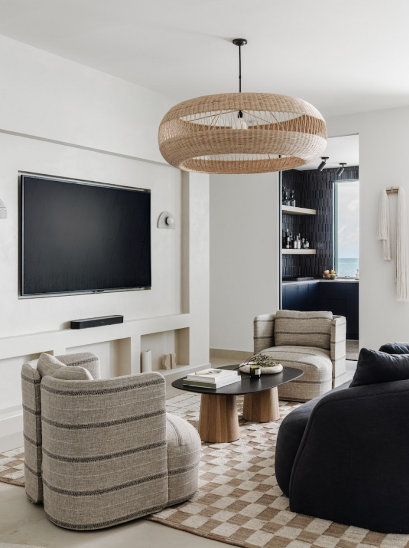 Media lounge with rattan chandelier, striped swivel chairs, and checkerboard rug in the Peaceful Waters home