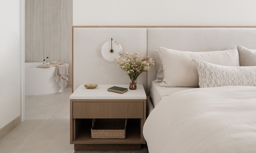 Nightstand styled with pink blossoms, a wall sconce, and woven basket in the Islamorada primary bedroom
