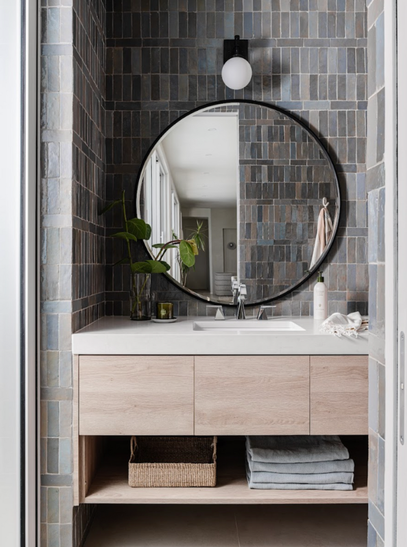 Powder bath with blue-gray zellige tile, round black mirror, and floating white oak vanity