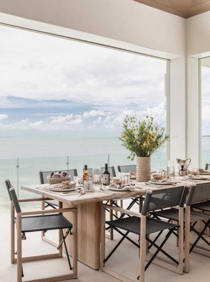 Covered terrace dining with wildflower centerpiece and black folding chairs above the sea at Peaceful Waters