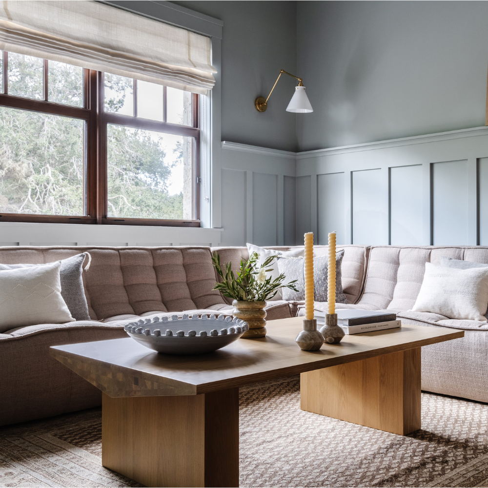 Slate-blue paneled living room with a taupe sectional and oak coffee table, featured in Coral Gables Magazine