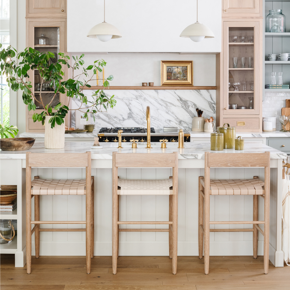 White oak counter stools at a marble kitchen island in the Calimia Home showroom, featured in Luxe Magazine