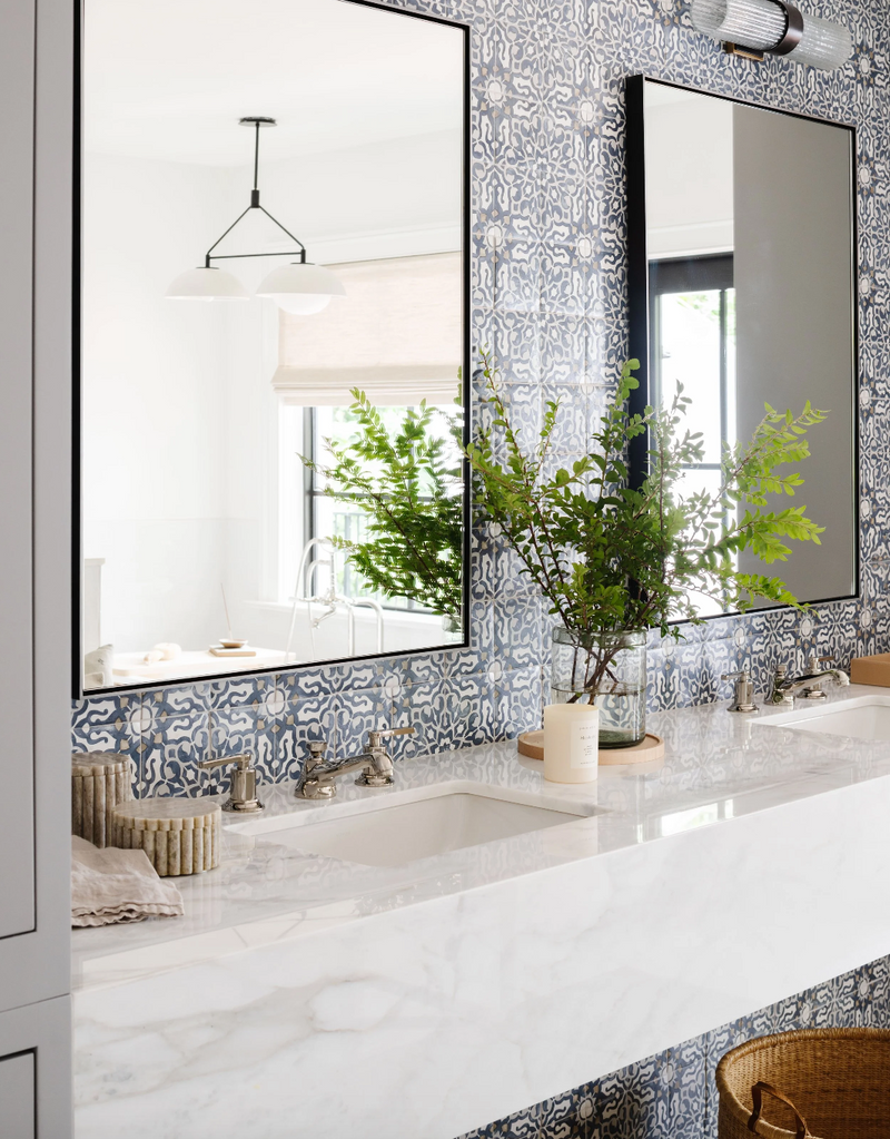 Bathroom with blue patterned tile wall, marble counter, and black-framed mirrors in this historic Miami renovation