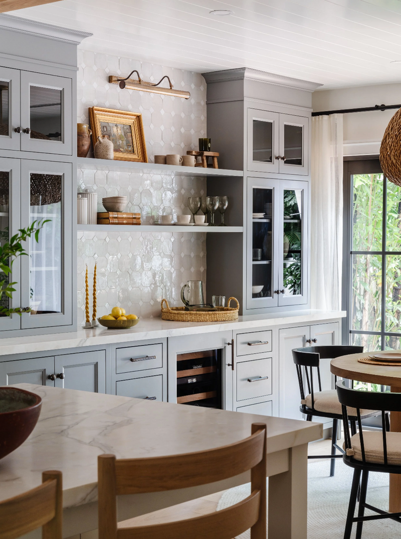 Breakfast corner with gray glass-front cabinets, patterned tile backsplash, and brass picture light