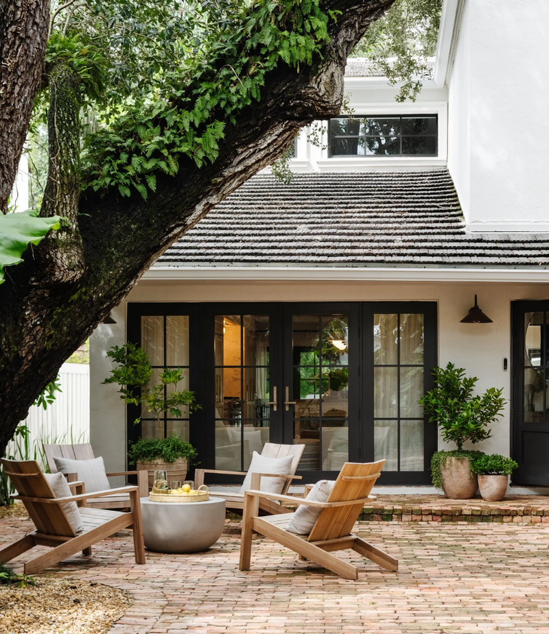 Brick courtyard with teak lounge chairs beneath a sprawling oak at the Raynolds Residence in Coconut Grove