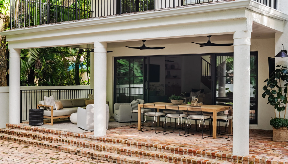 Covered outdoor dining porch with ceiling fans and brick steps beneath an upper balcony