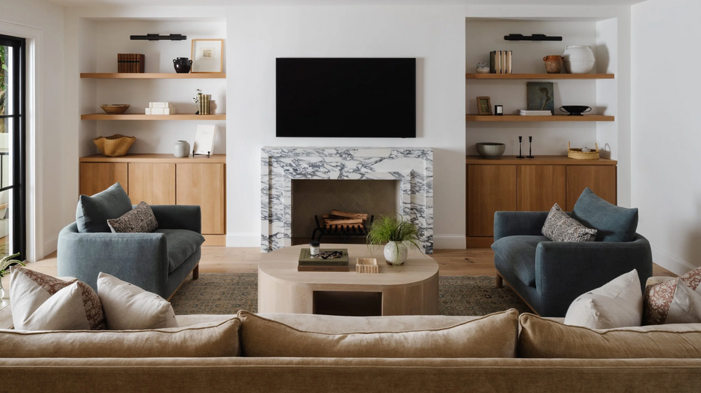 Family room with marble fireplace, built-in oak shelving, and a pair of navy armchairs