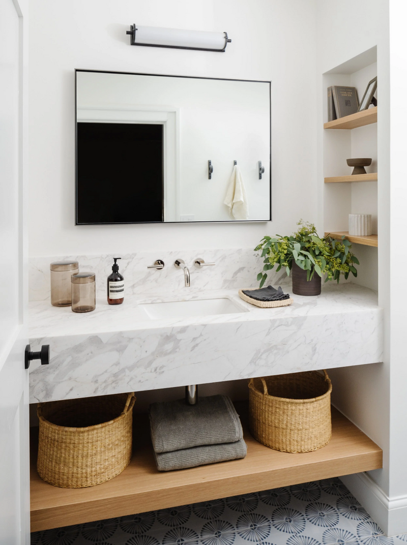 Floating marble vanity with wall-mount faucet, woven baskets, and oak shelving in the Raynolds Residence