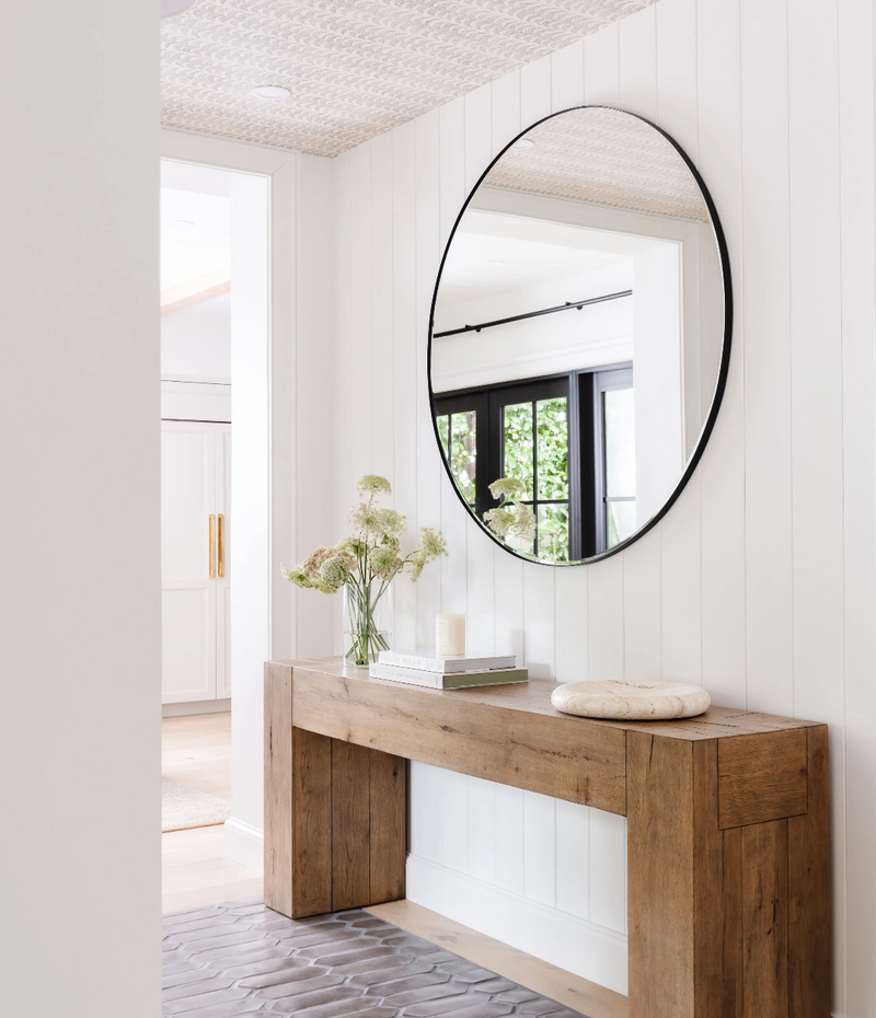 Hallway with round black mirror, chunky wood console table, and vertical shiplap paneling