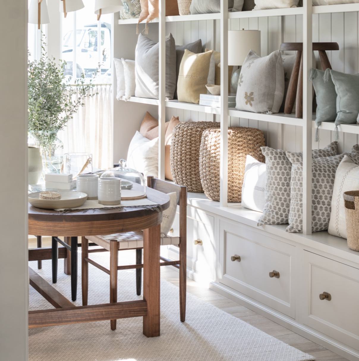 Calimia Home showroom display with built-in white shelving styled with neutral throw pillows and woven poufs.