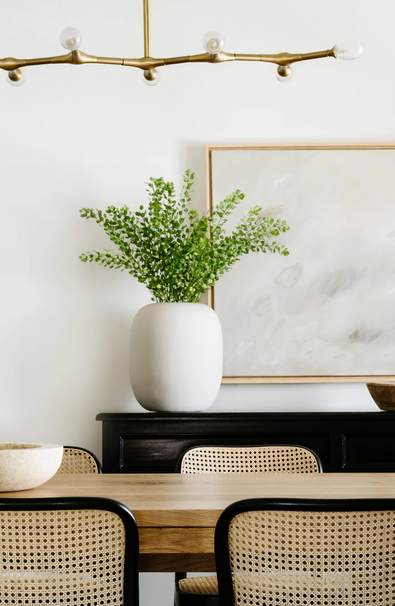 Dining room vignette with abstract art, black sideboard, and cane-back chairs