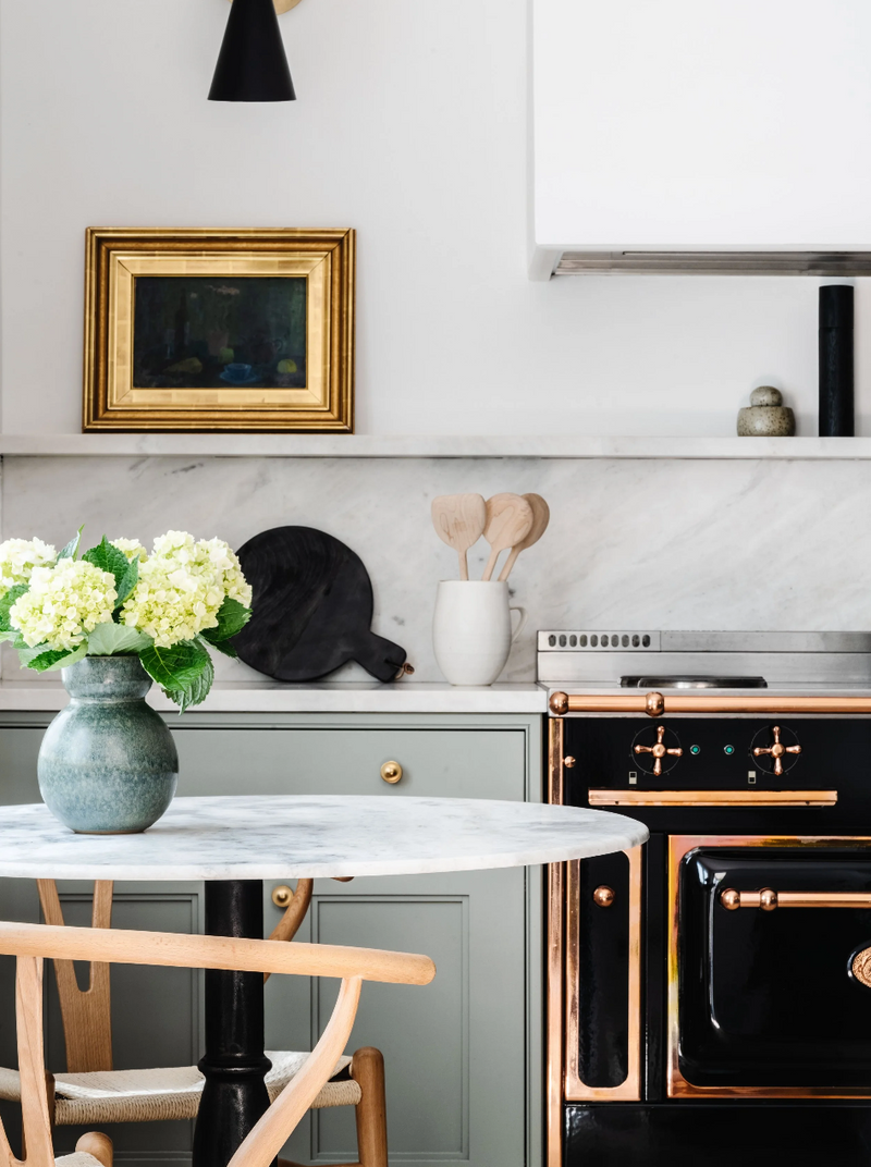 Marble bistro table with hydrangeas beside a black French range and gilt-framed art