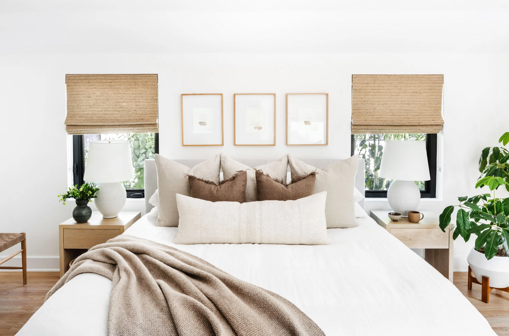 Serene primary bedroom with woven shades, framed botanical art, and layered neutral bedding