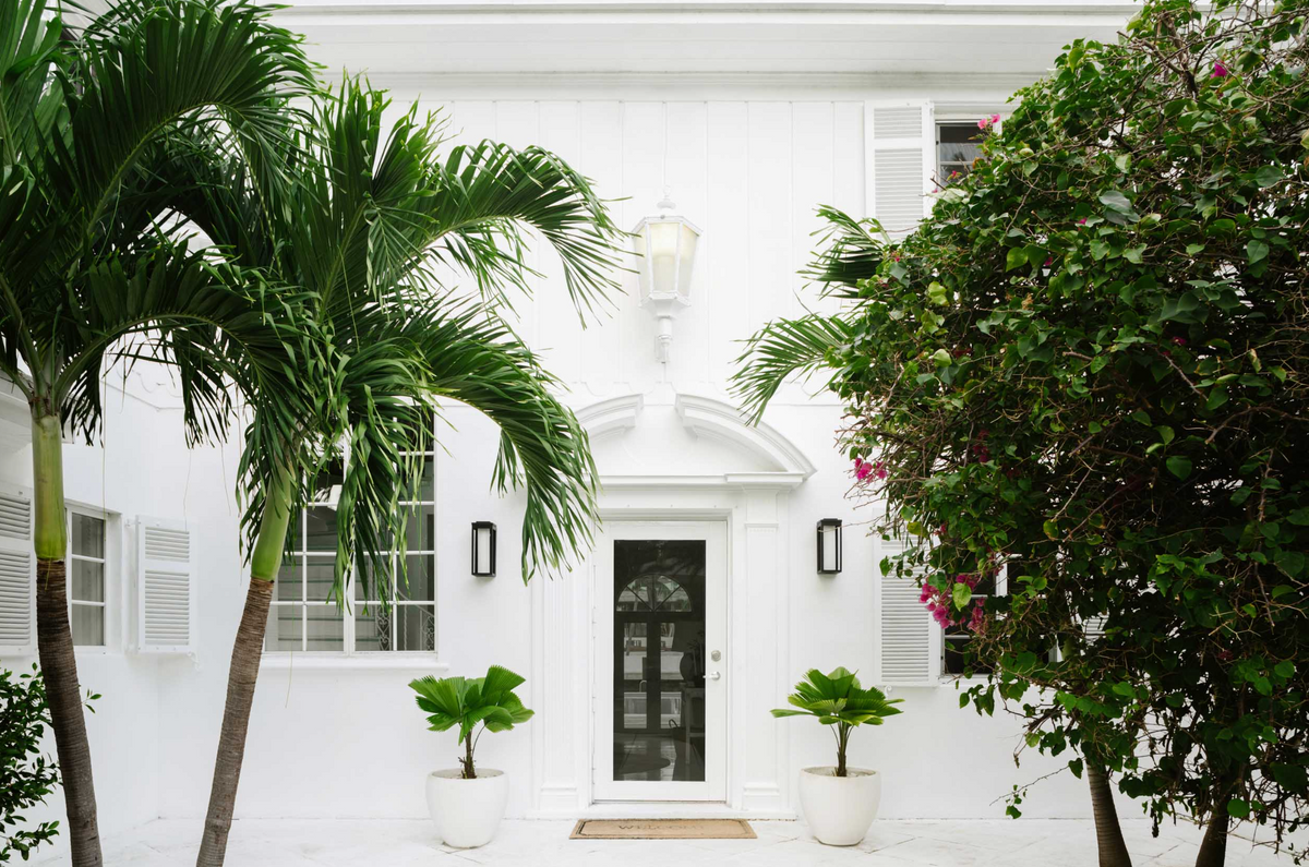 Glossy black front door flanked by lanterns and potted topiaries at this Sunset Island entry