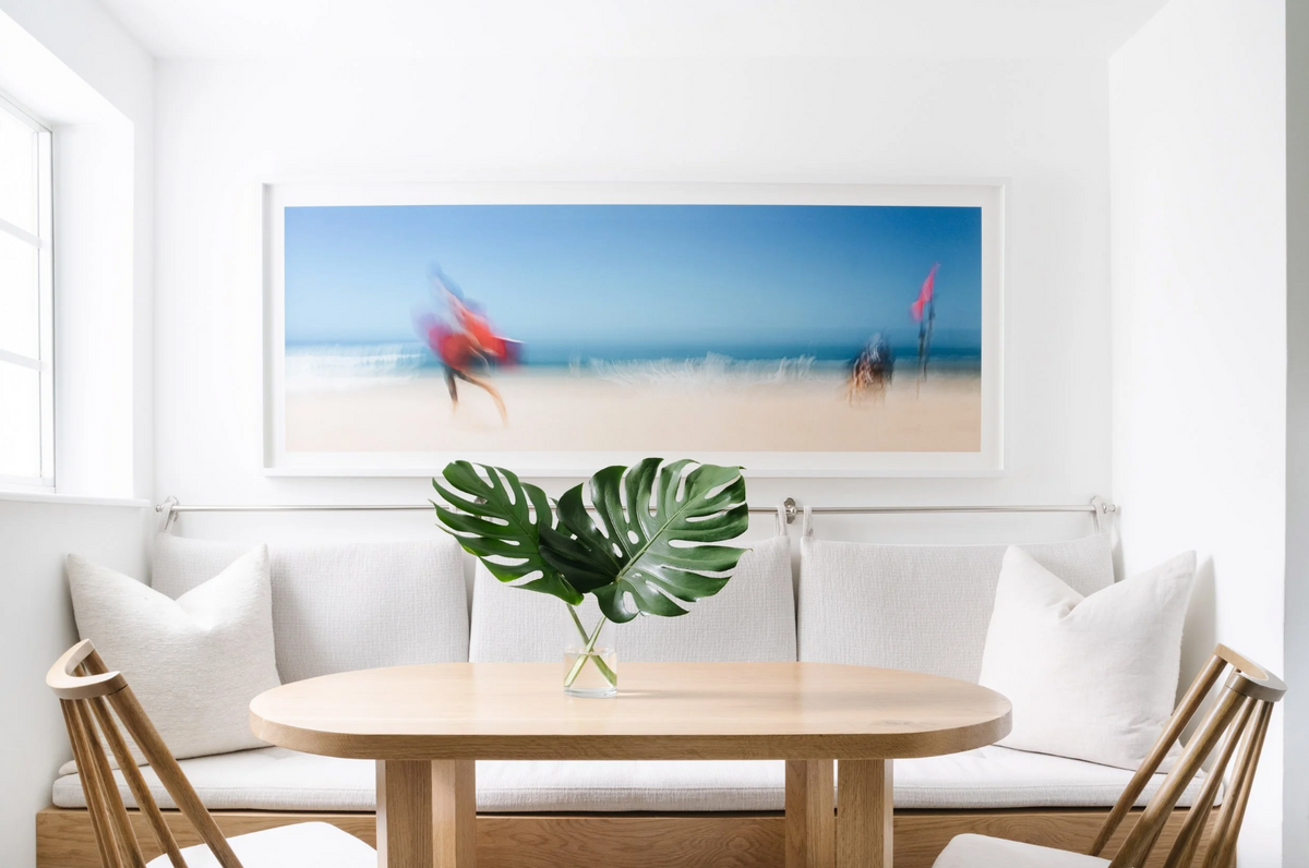Breakfast nook with oval oak table, banquette seating, and beach photography in the Sunset Island residence