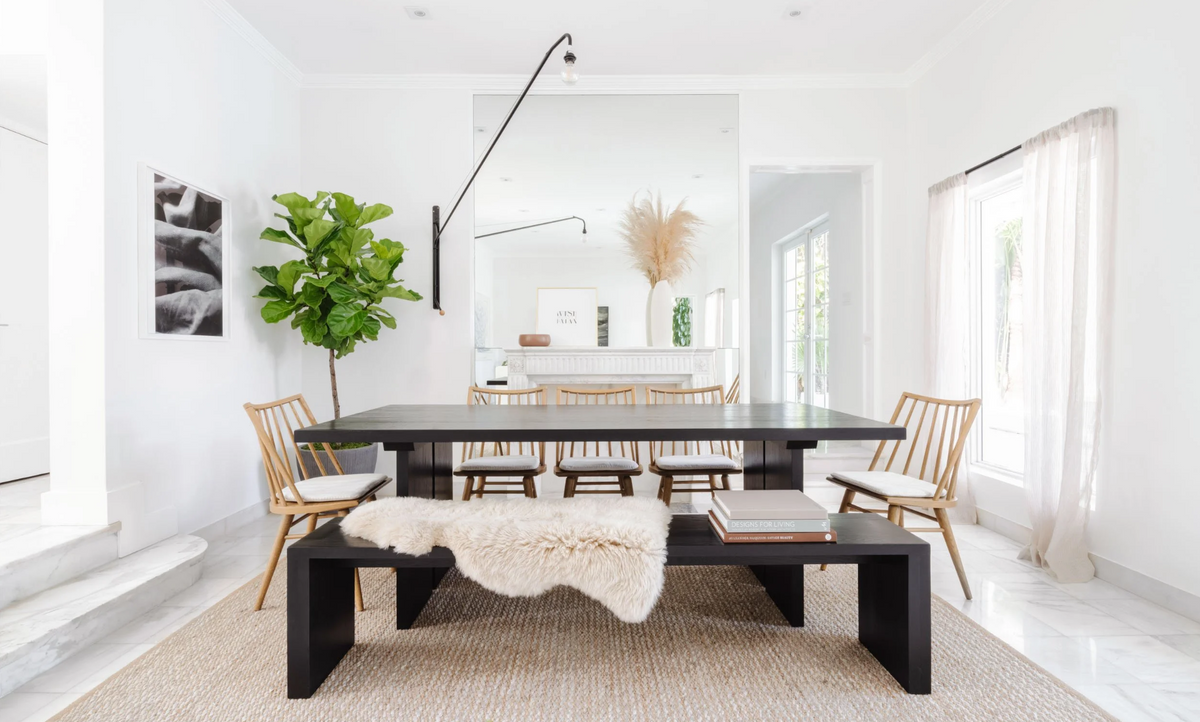 Minimal dining room with black table, woven chairs, and layered rugs beneath a sculptural light