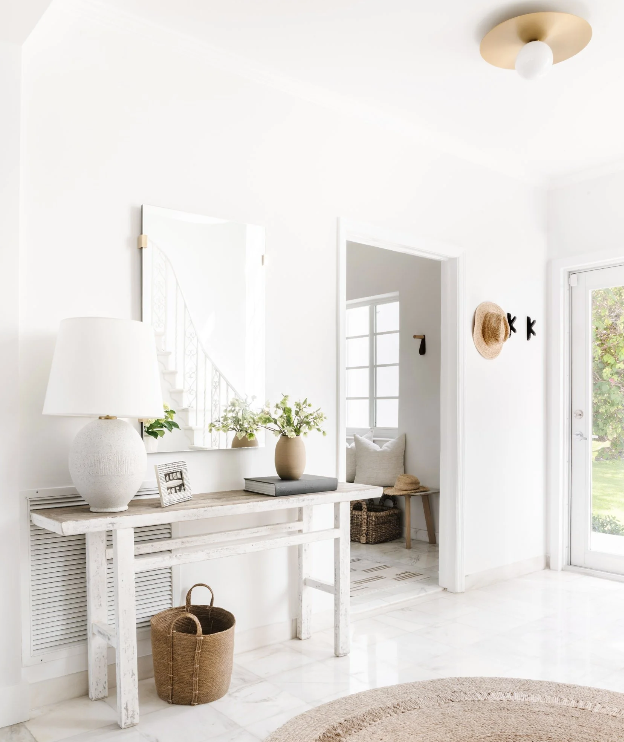 Sunlit entry with whitewashed console, ceramic lamp, and woven baskets in this Miami Beach home