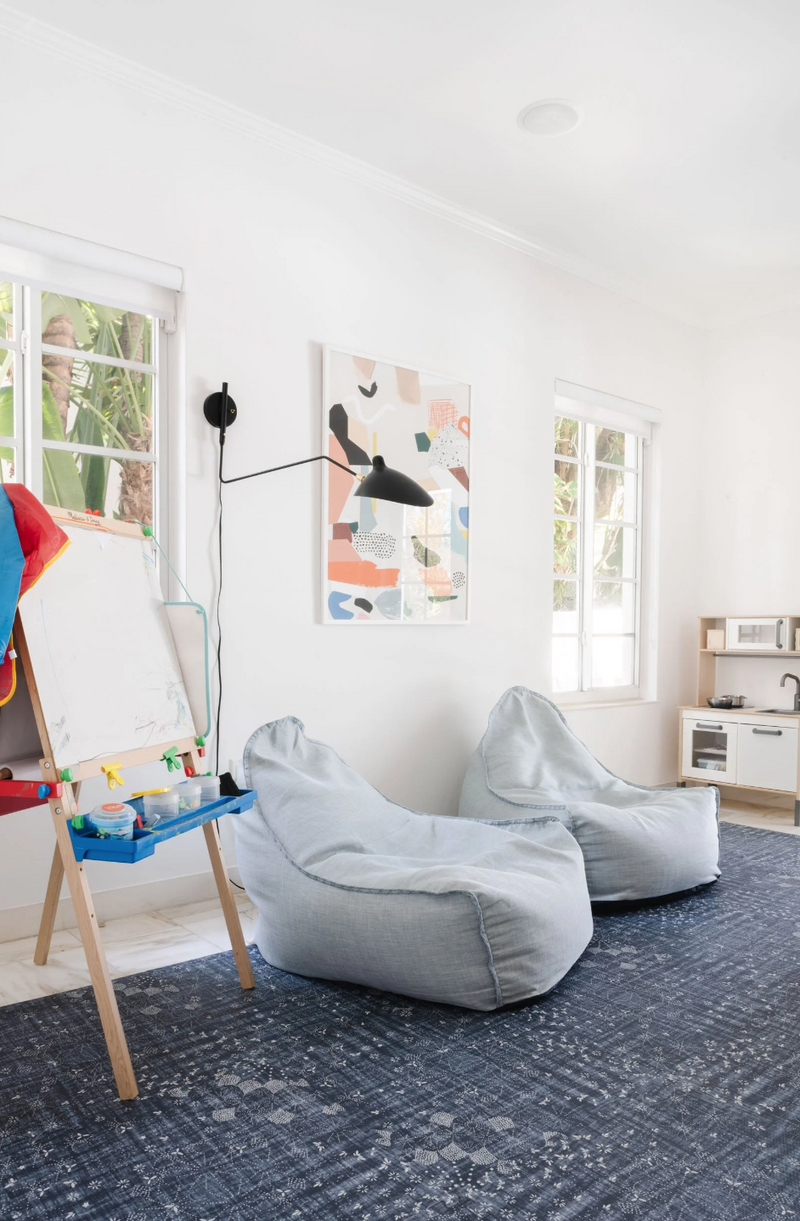 Kids' playroom with art easel, gray beanbag chairs, and play kitchen on a patterned blue rug