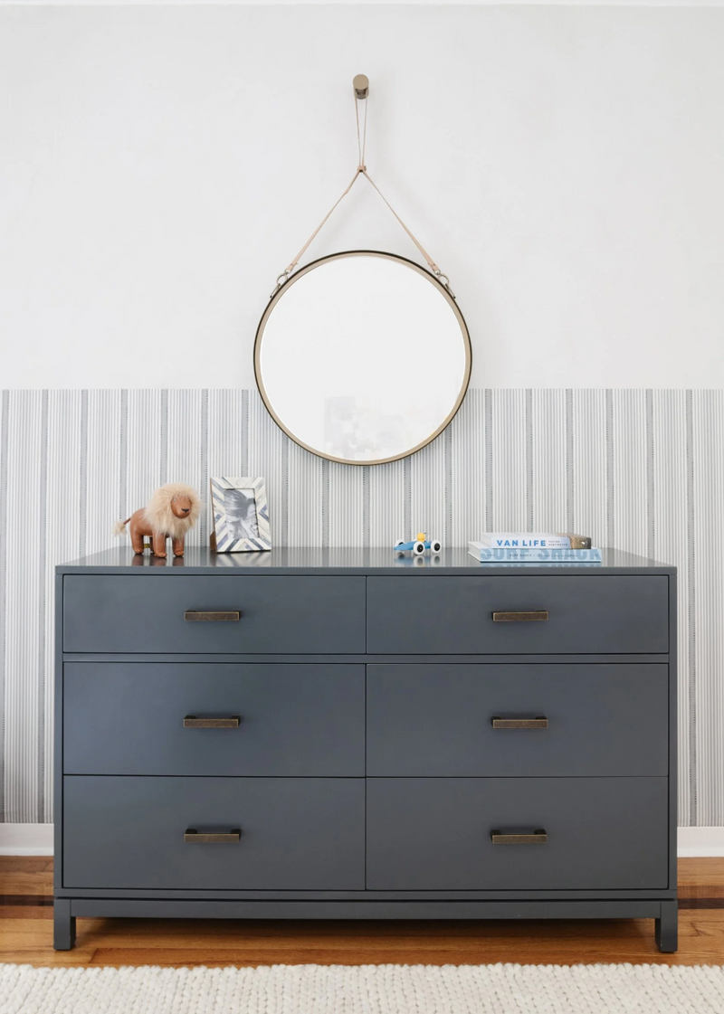 Navy six-drawer dresser under a round leather-strap mirror in this Miami Beach kids' room