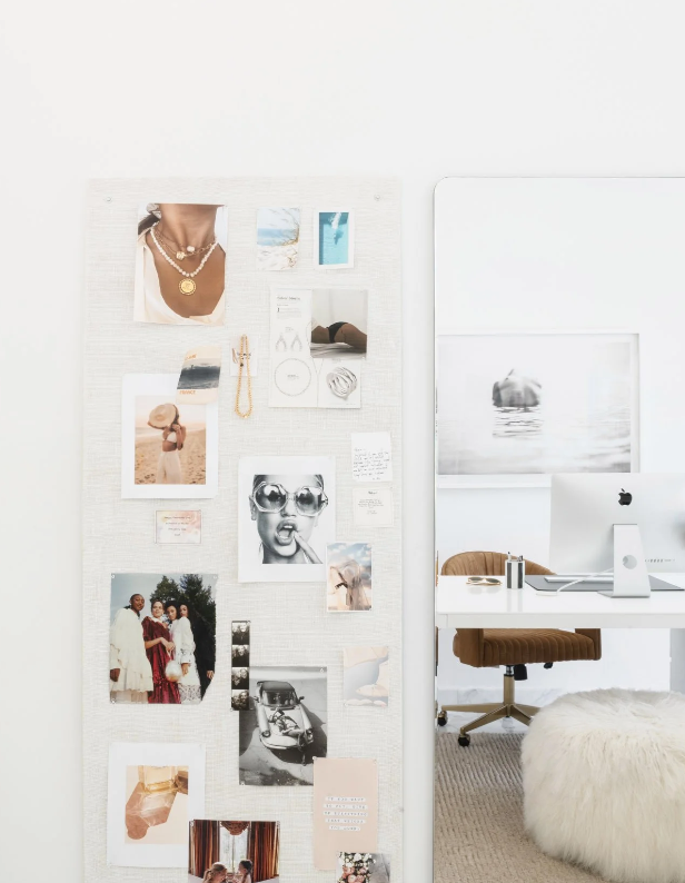 Linen pinboard layered with jewelry and photographs beside a sunlit home office desk
