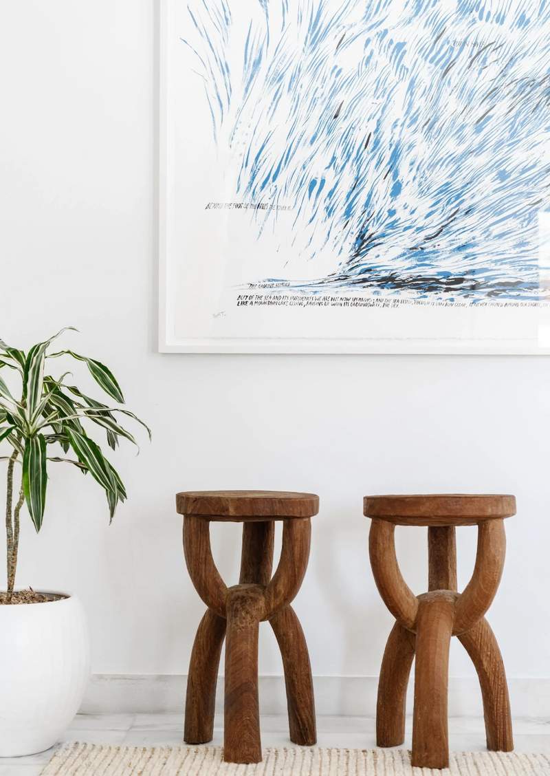 Pair of carved wooden tripod stools beneath blue abstract art in the Sunset Island residence