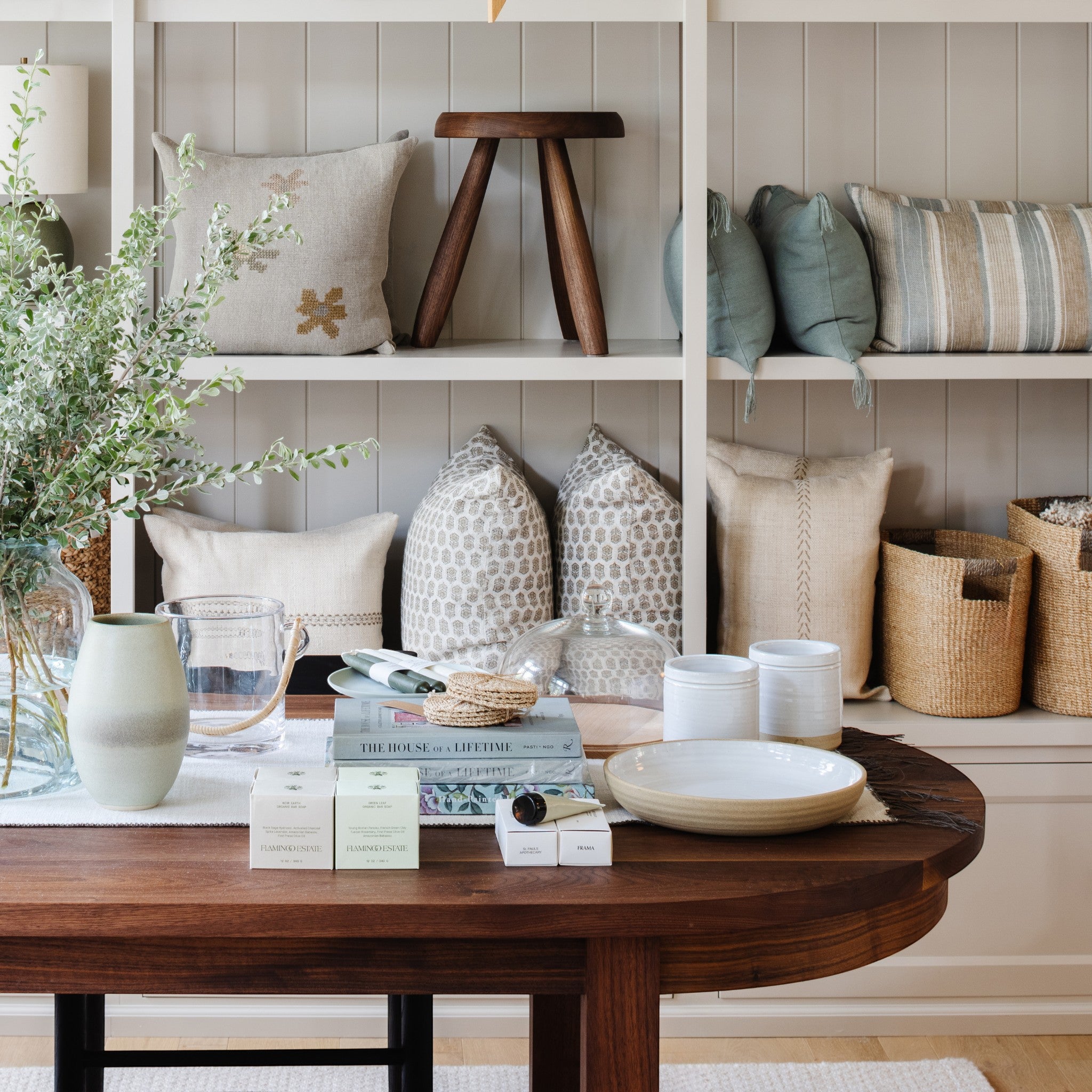 Calimia Home Tori Stool with three tapered legs and a round top, displayed on a wooden shelf in a cozy living room.