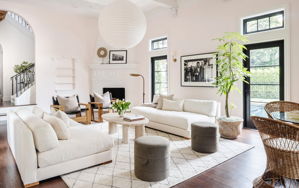 Modern living room with white furniture, plants, and large windows.