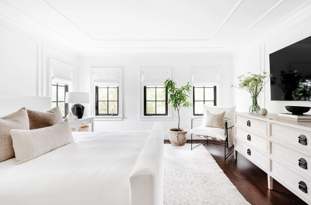 Modern bedroom with white furniture, plants, and a television.