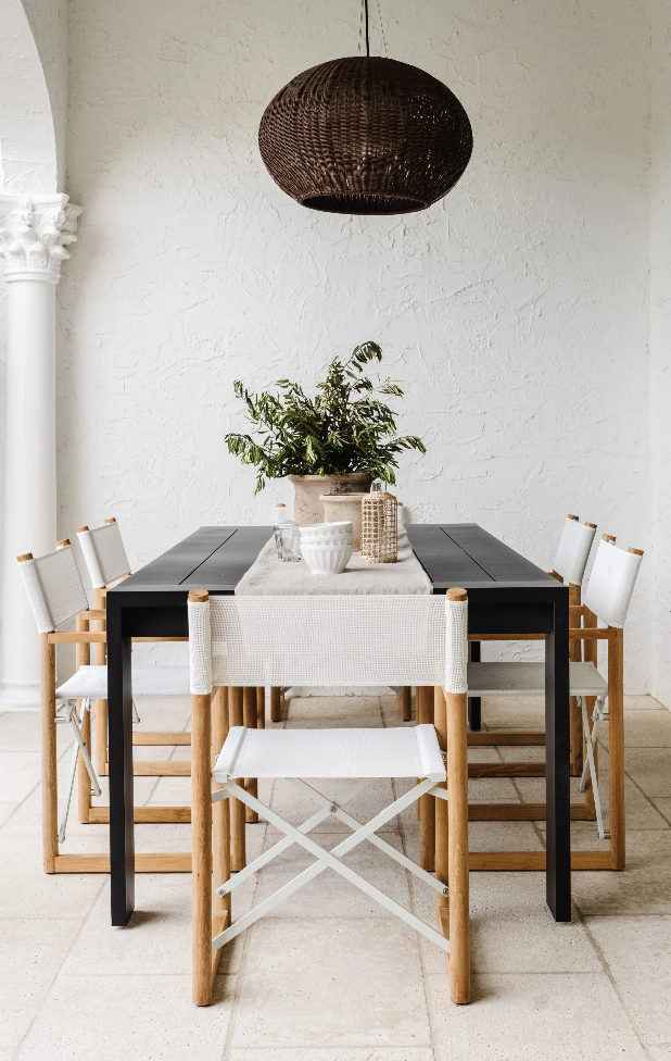 Outdoor dining area with black table, white sling chairs, and woven pendant at Villa Belmonte