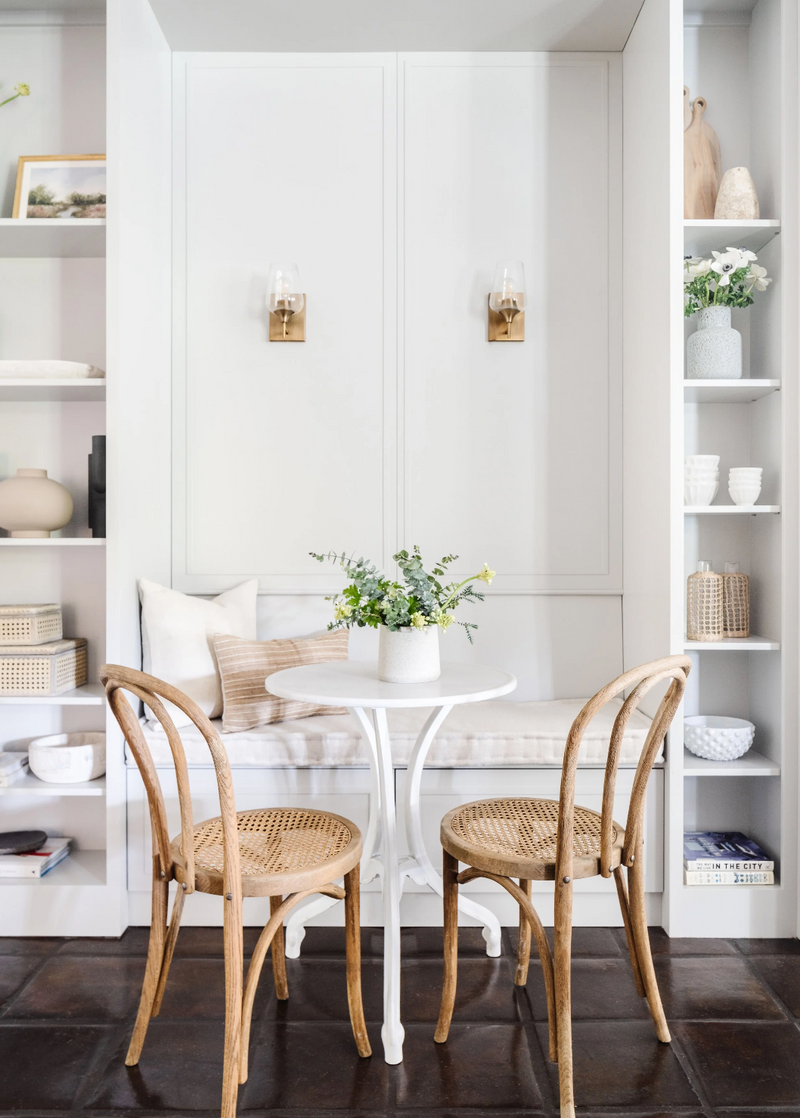 Small dining area with a white table and two wooden chairs against a white wall.