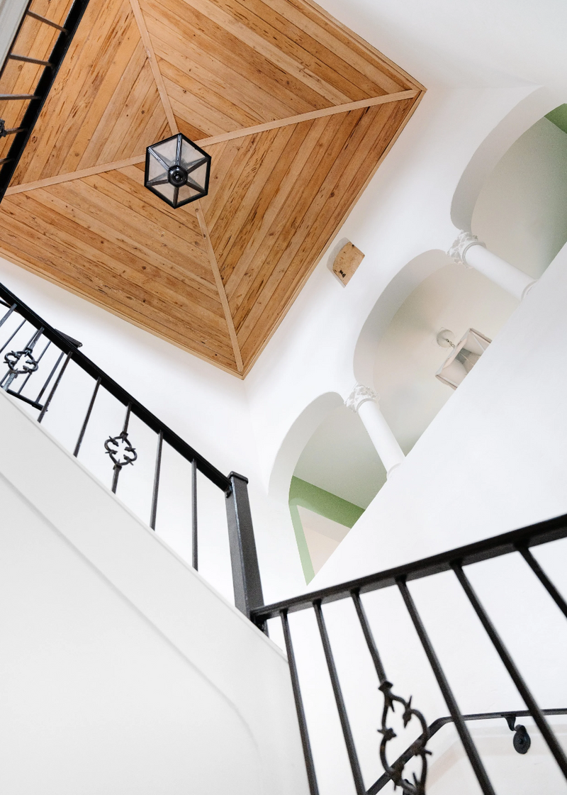 Looking up a stairwell at a wood-paneled ceiling, lantern pendant, and wrought iron railing