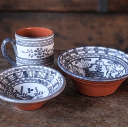 Calimia Home hand-thrown ceramic bowls and mug with grey floral glaze and terracotta base on a rustic wooden table.