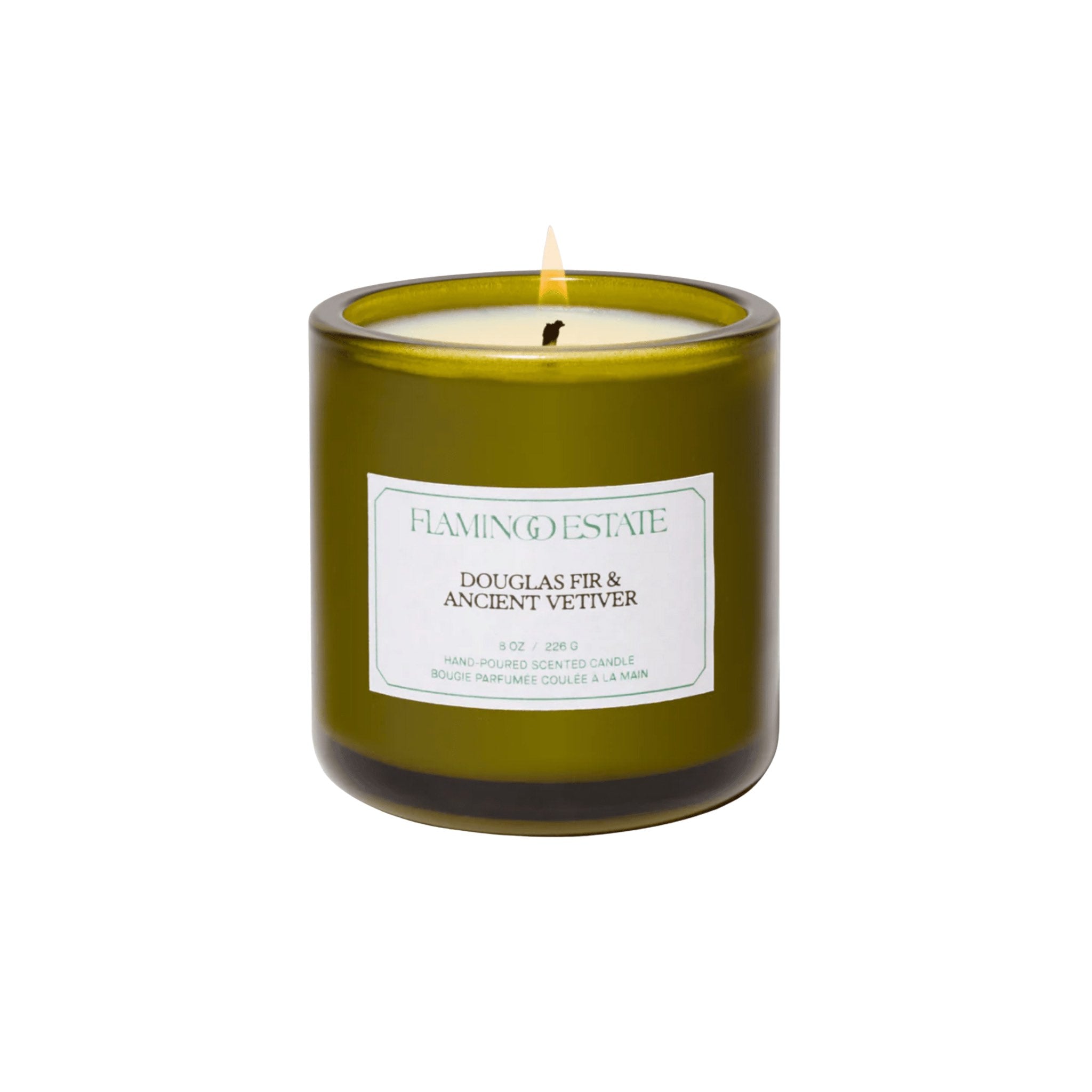 A Flamingo Estate Douglas Fir & Ancient Vetiver Candle in an olive-green glass jar with a seafoam label, on a white background.