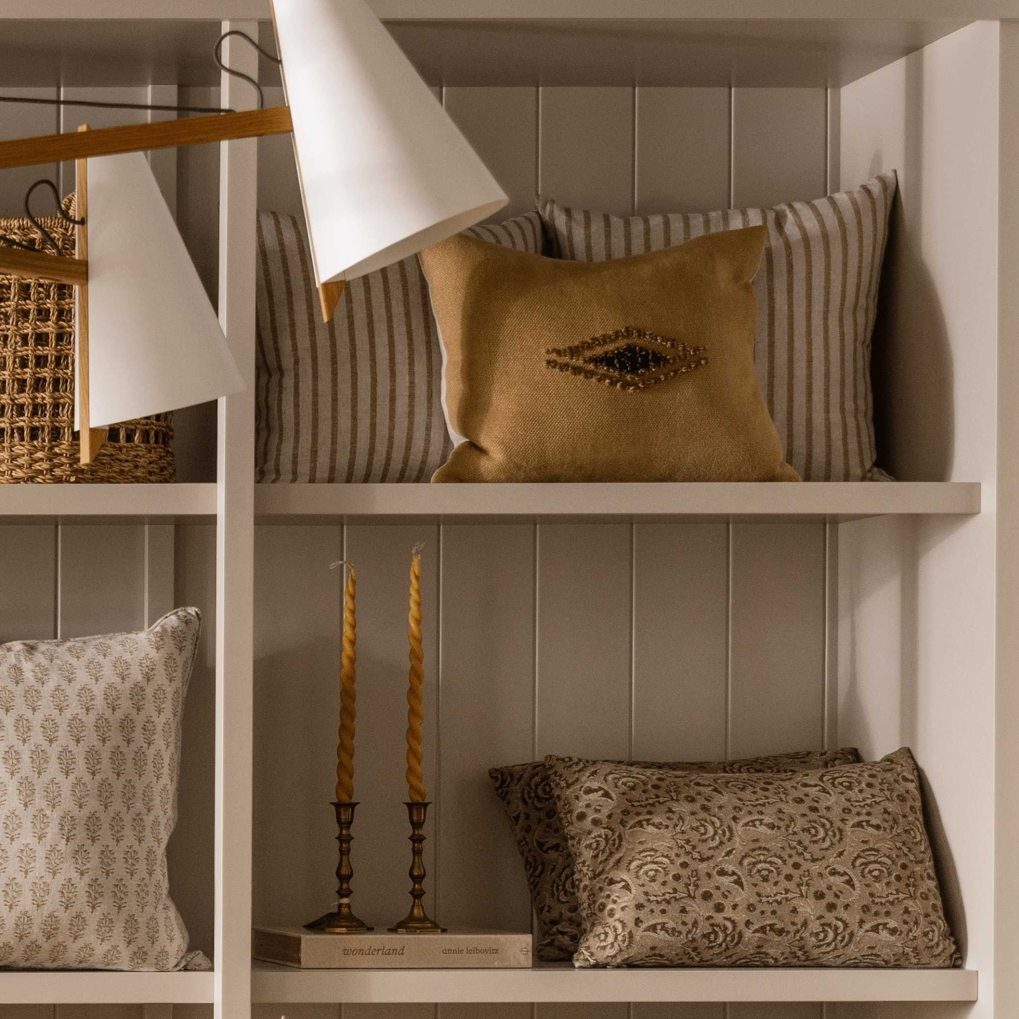 Calimia Home Eira mustard linen pillow with hand-embroidered wool eye motif displayed on a white shelf