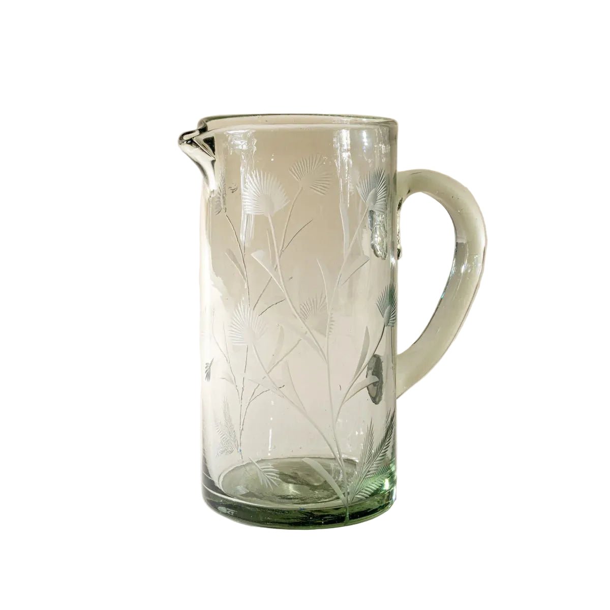 Clear glass pitcher with floral etching on a beige background