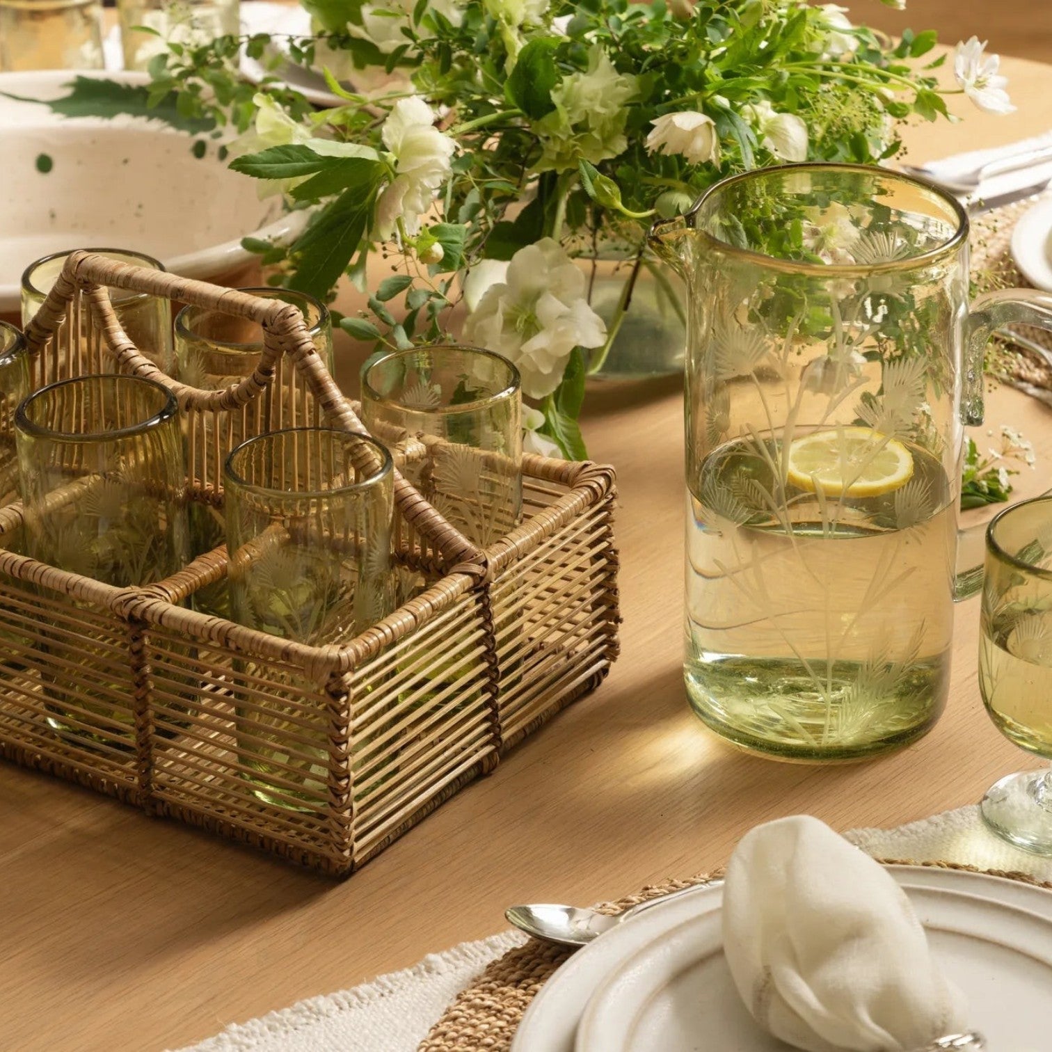 Calimia Home olive recycled glass pitcher with delicate etched thistle design on a dining table with rattan caddy