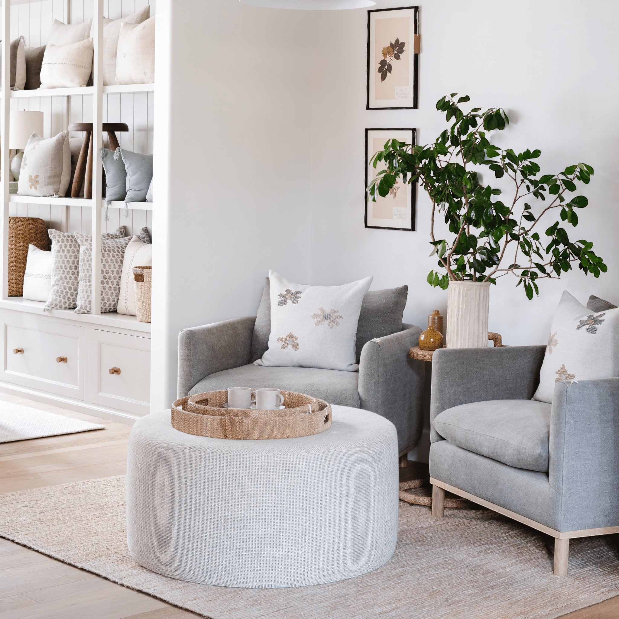 Calimia Home Fenn chairs in grey linen with natural oak legs and a matching round ottoman in a bright living room.